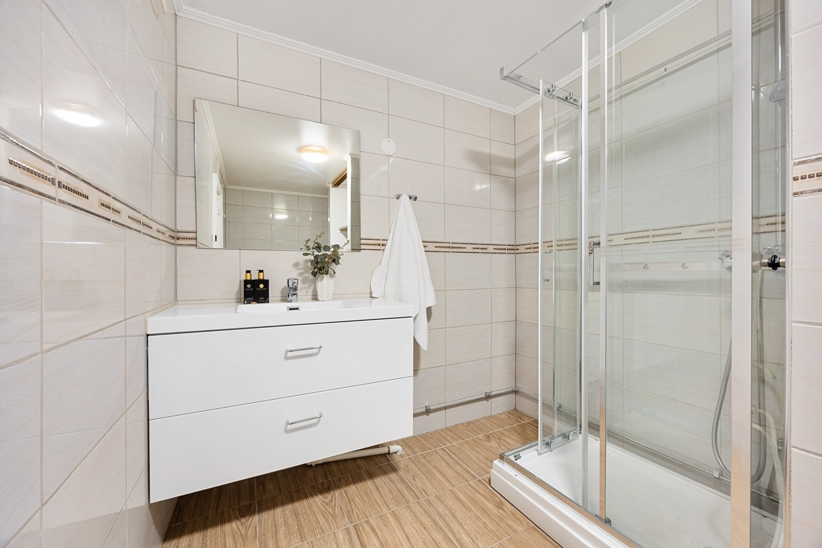 Badet har vegghengt servantinnredning og et dusjhjørne med innfellbare glassdører. Galleribilde