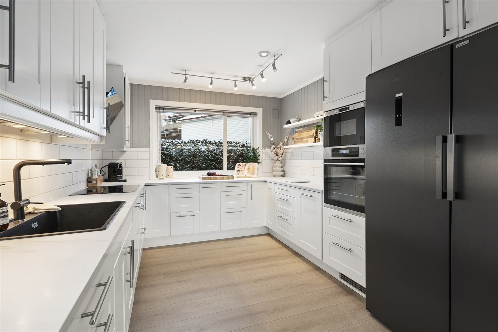 Kjøkkenet er holdt i en tidløs stil med hvite, profilerte fronter. Det ble oppgradert i 2023 med ny benkeplate i laminat og en moderne sort komposittvask. Galleribilde