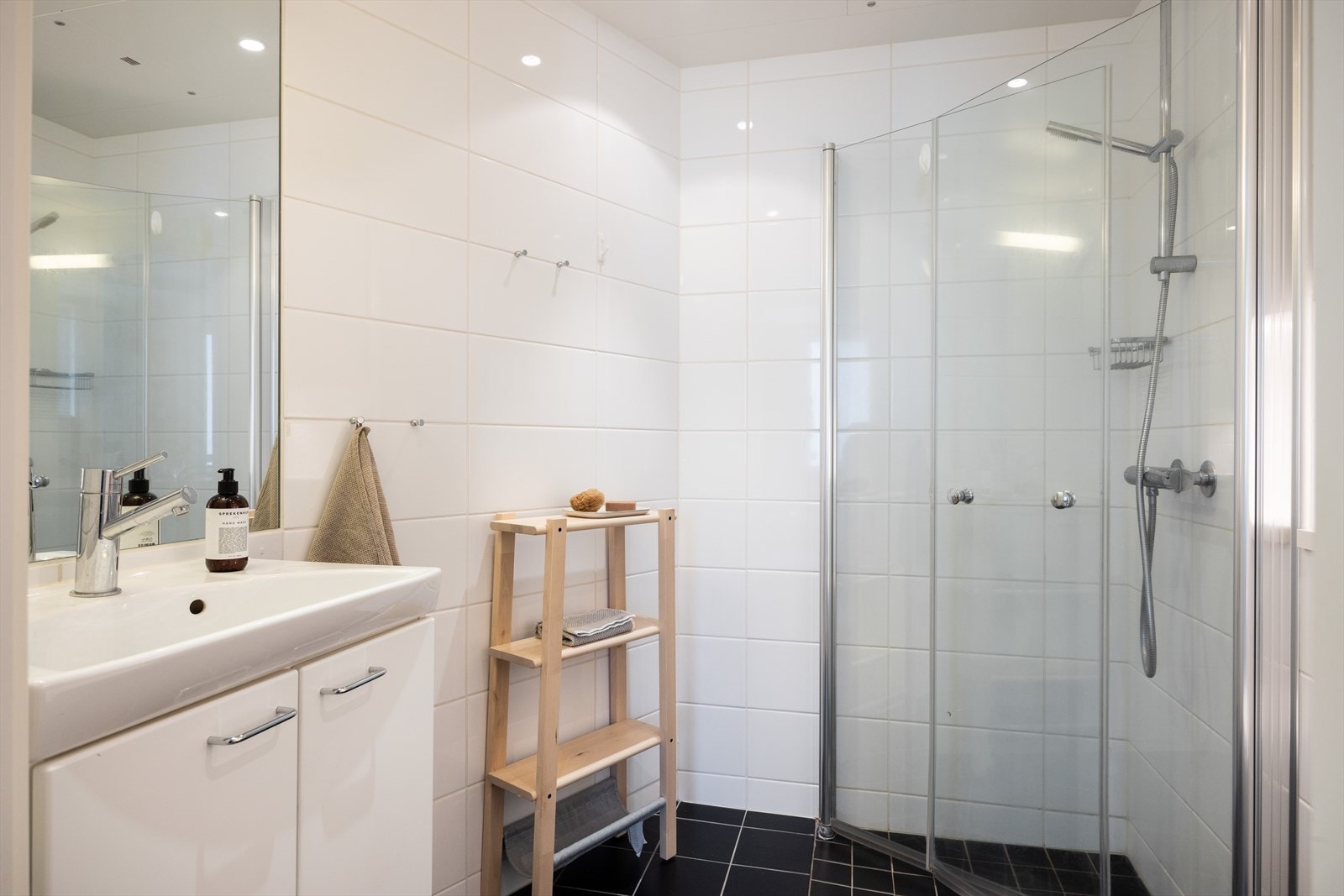 Pent, flislagt baderom med downlights i himlingen og elektriske varmekabler. Badet er innredet med veggmontert toalett, dusjhjørne med vegg og dør i herdet glass, servant, skap, speil og belysning. Det er opplegg for vaskemaskin. Galleribilde