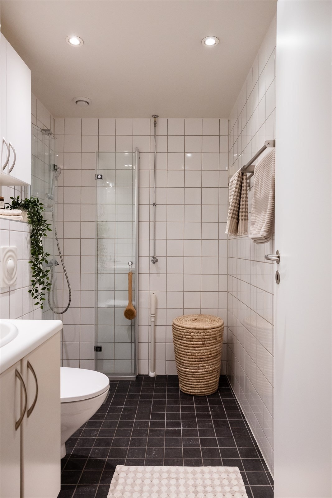 Innredning bestående av bl.a. servantskap med nedfelt servant og underskap med glatte fronter, speil og lysarmatur på vegg over servant, veggmontert klosett og dusjhjørne med foldedører. Galleribilde