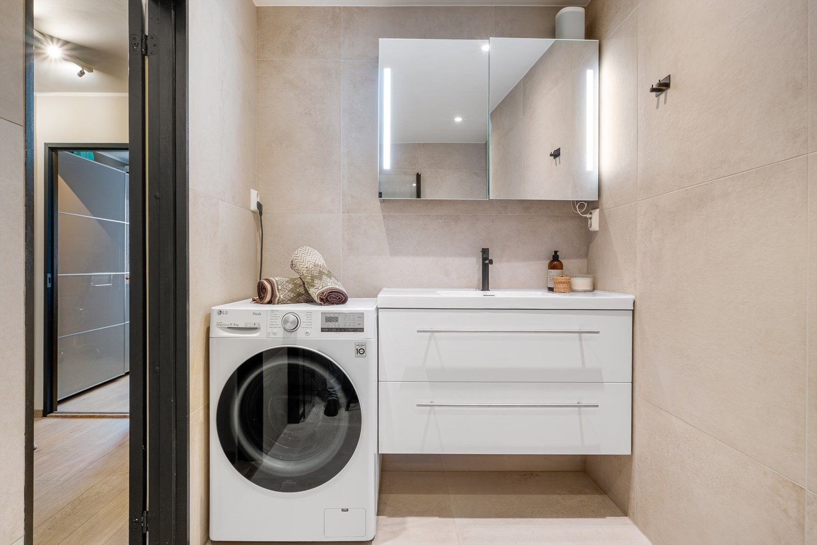 Badet er utstyrt med vegghengt toalett med innebygget sisterne, servant med underskap, speilskap med belysning og et skjermet dusjhjørne med herdet glass. Galleribilde