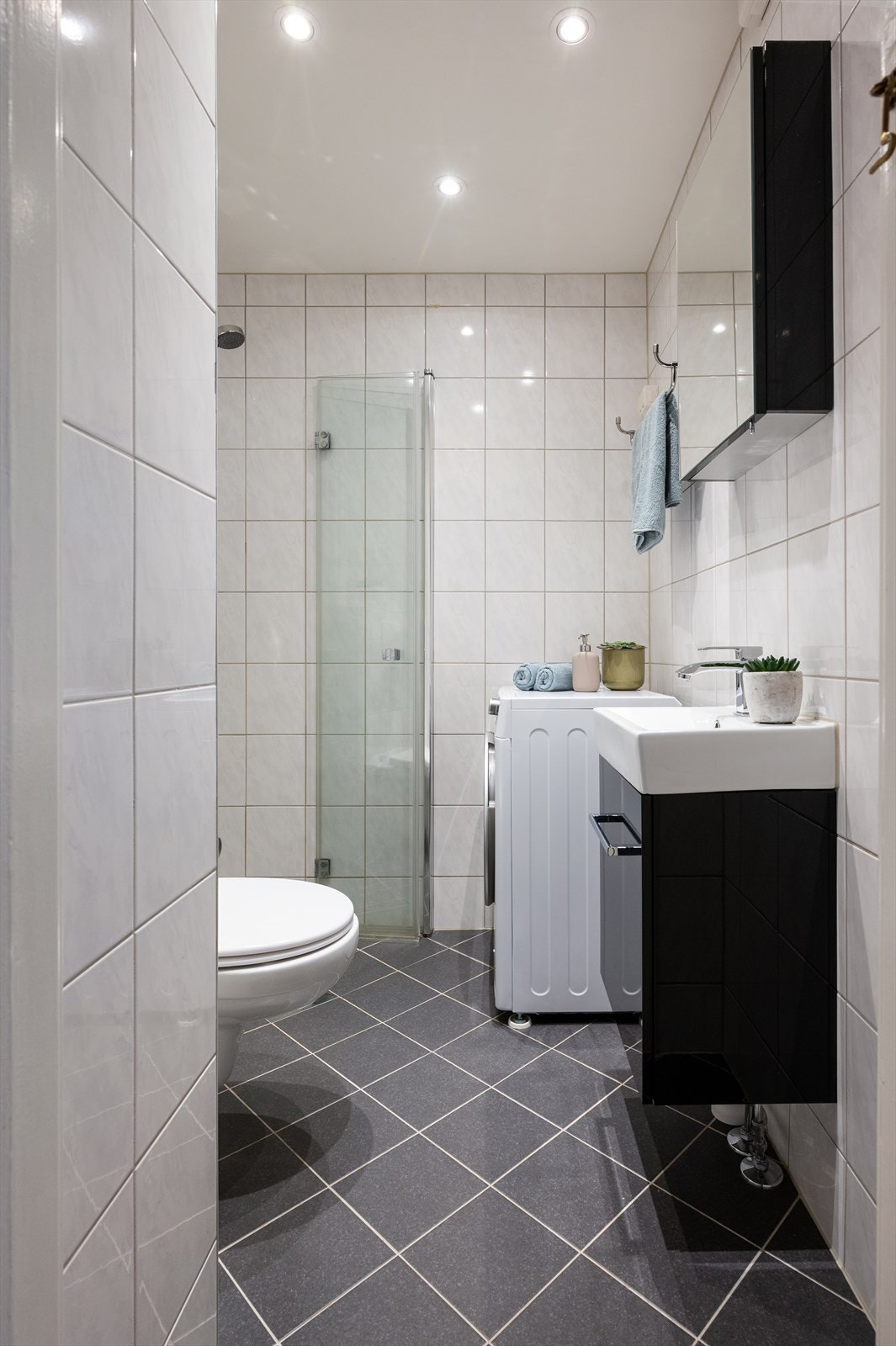 Flislagt baderom av god størrelse, innredet med dusjhjørne med innfellbare glassdører, heldekkende servant på underskap, speil og belysning. Galleribilde