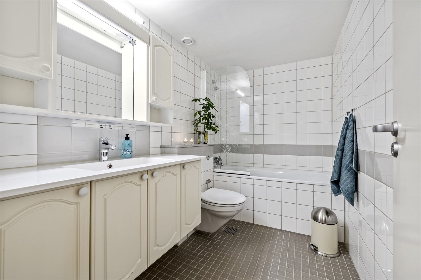 Badet har flislagt gulv med varmekabler, badekar med dusjvegg og veggmontert toalett. Galleribilde