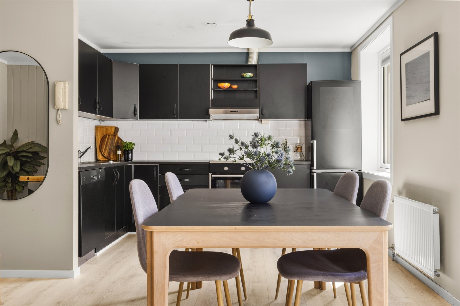 Stilren og moderne kjøkkenløsning med svarte fronter, lyse gulv og god spiseplass i naturlig lys fra store vindusflater. Galleribilde