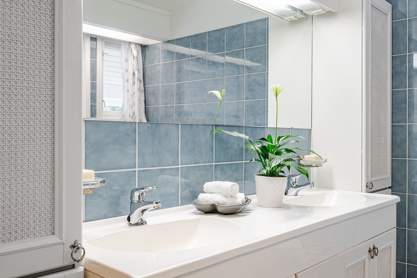 Lys baderomsinnredning med heldekkende dobbel servant, speil med belysning over og høyskap på begge sider. Galleribilde