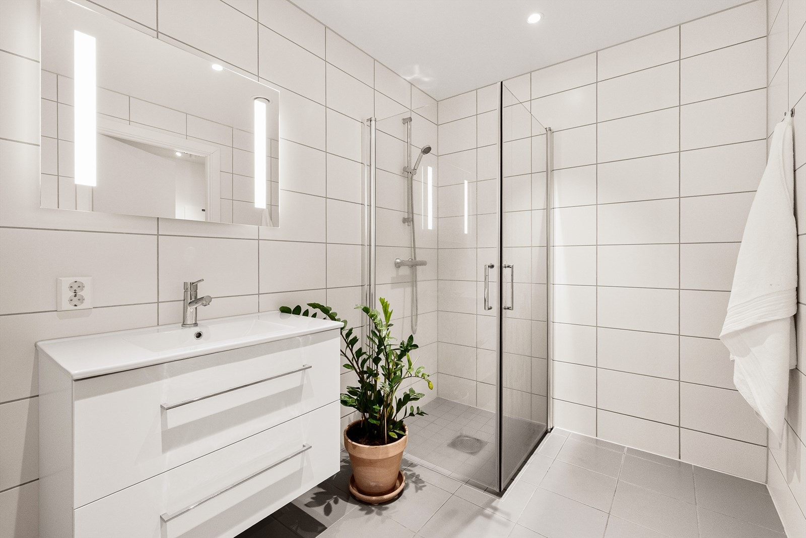 Taket har malte, slette flater, og badet er innredet med nedfelt servant, veggmontert toalett og dusjløsning med dusjdører/hjørne. Galleribilde