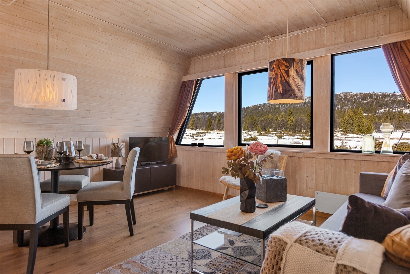 Hyttas hovedrom er stue og kjøkken i åpen løsning. Her er det lyst og trivelig med mange store vinduer og sjarmerende skråtak. Galleribilde