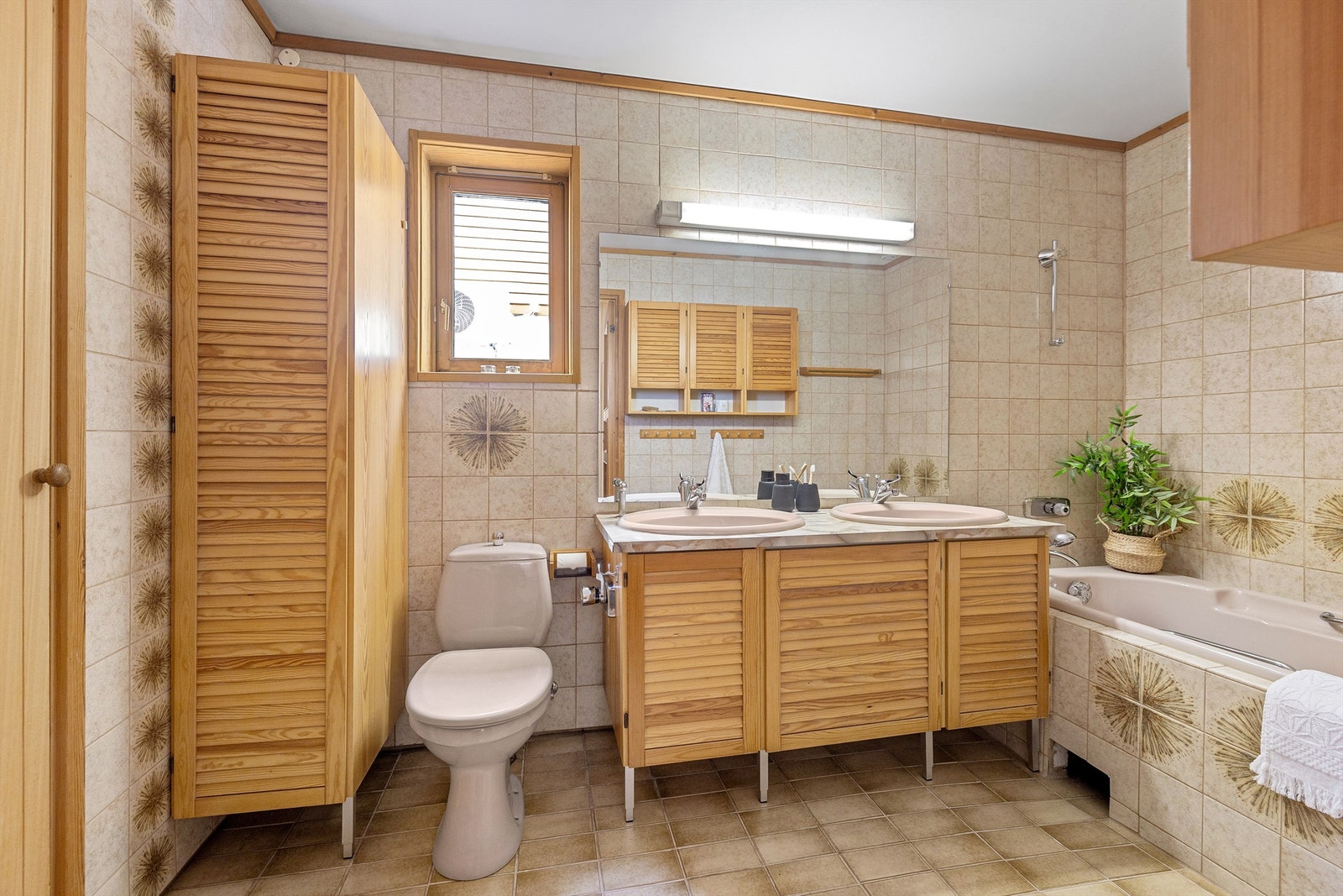 Badet er innredet med badekar, toalett, doble servanter og rikelig med baderomsinnredning Galleribilde