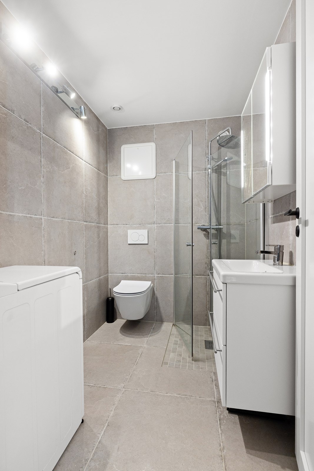 Delikat flislagt bad med gulvvarme, vegghengt toalett, innfellbare dusjvegger i glass, vegghengt baderomsinnredning og opplegg for vaskemaskin Galleribilde