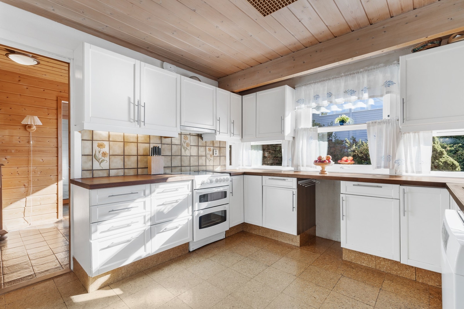 Kjøkkeninnredning med profilerte fronter fra byggeår, benkeplate i heltre og fliser på vegg mellom benkeplate og overskap Galleribilde