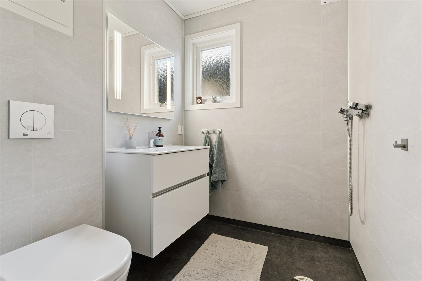 Bad i 1.etasje med servantinnreiing og vegghengt toalett. Her er det belegg på golv med varmekablar og baderomsplater på vegg. Galleribilde