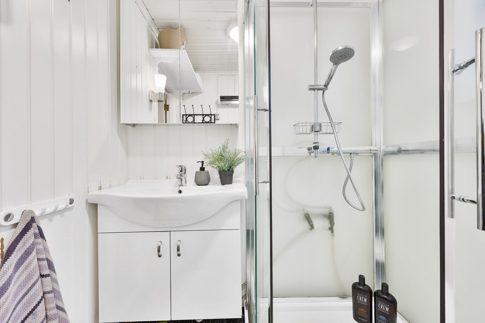 Innredningen har heldekkende servant over skapseksjon, i overkant er det dobbelt speilskap. Videre har badet dusjkabinett med buede skyvedører og toalett. Galleribilde