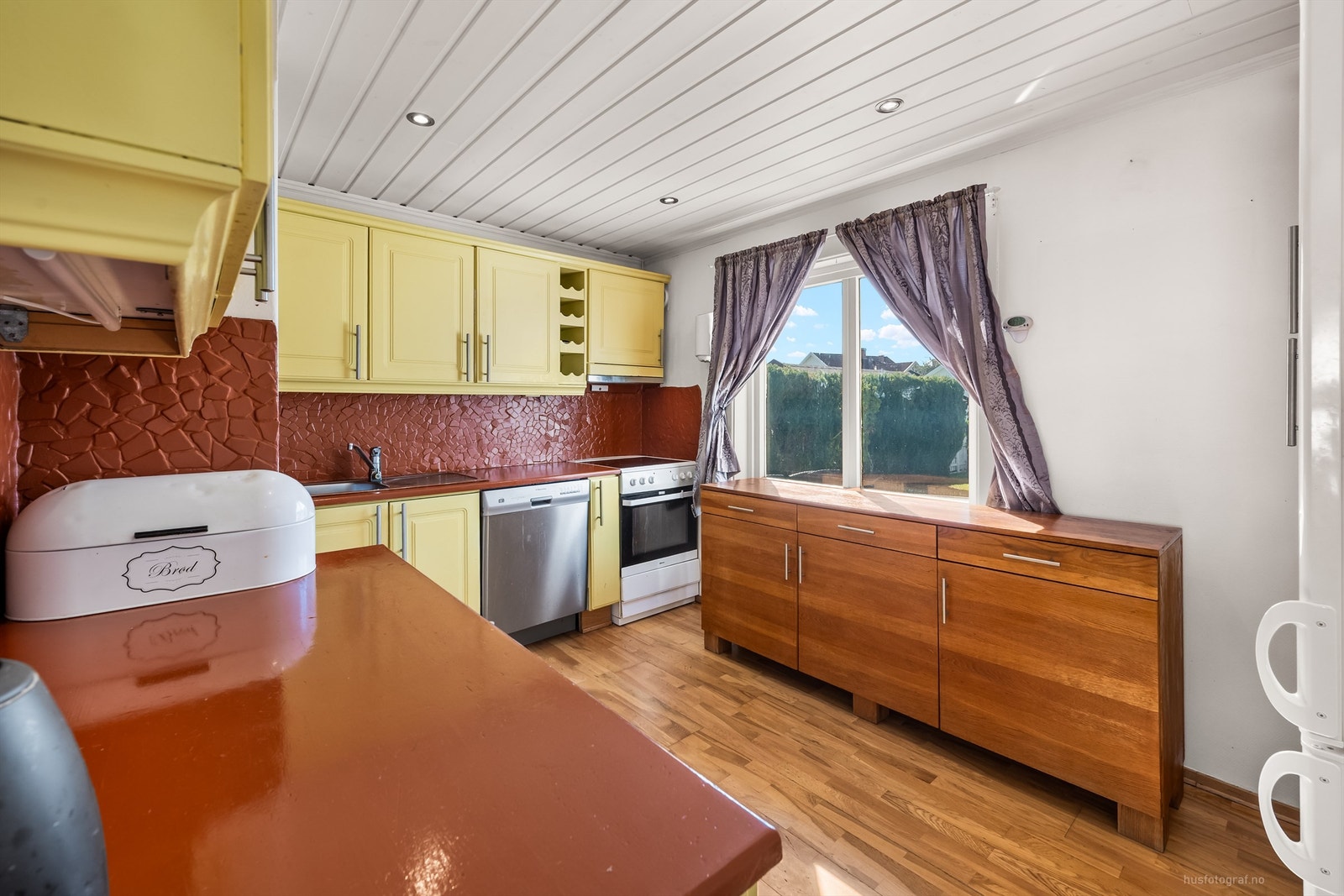 Mellom benkeplaten og overskapene er det lagt fliser som både beskytter og tilfører et dekorativt preg. Løsningen er praktisk med plass til frittstående hvitevarer Galleribilde