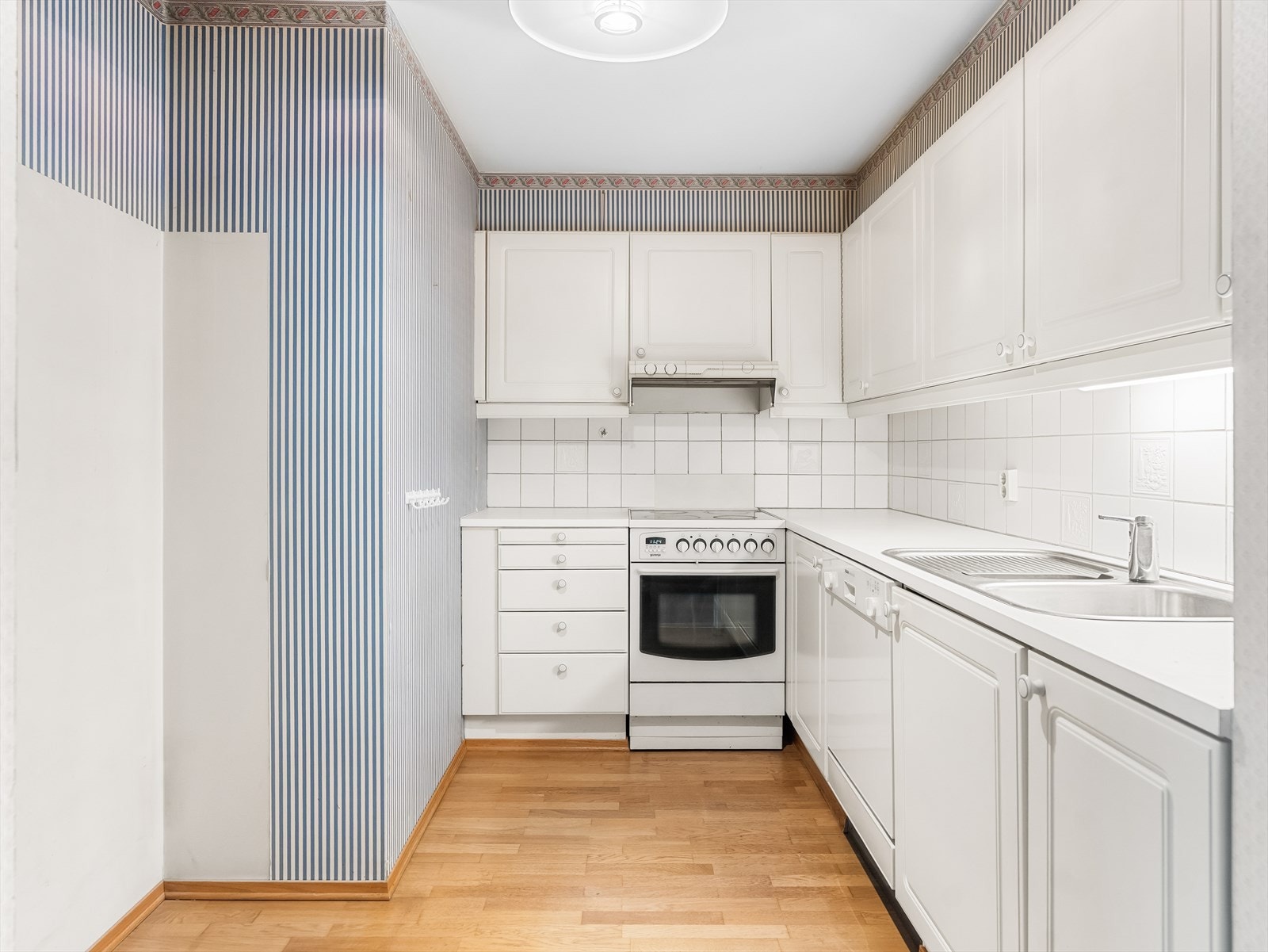 Kjøkkeninnredningen har skap med profilerte fronter, samt en laminat benkeplate med nedfelt kum i rustfritt stål. Galleribilde