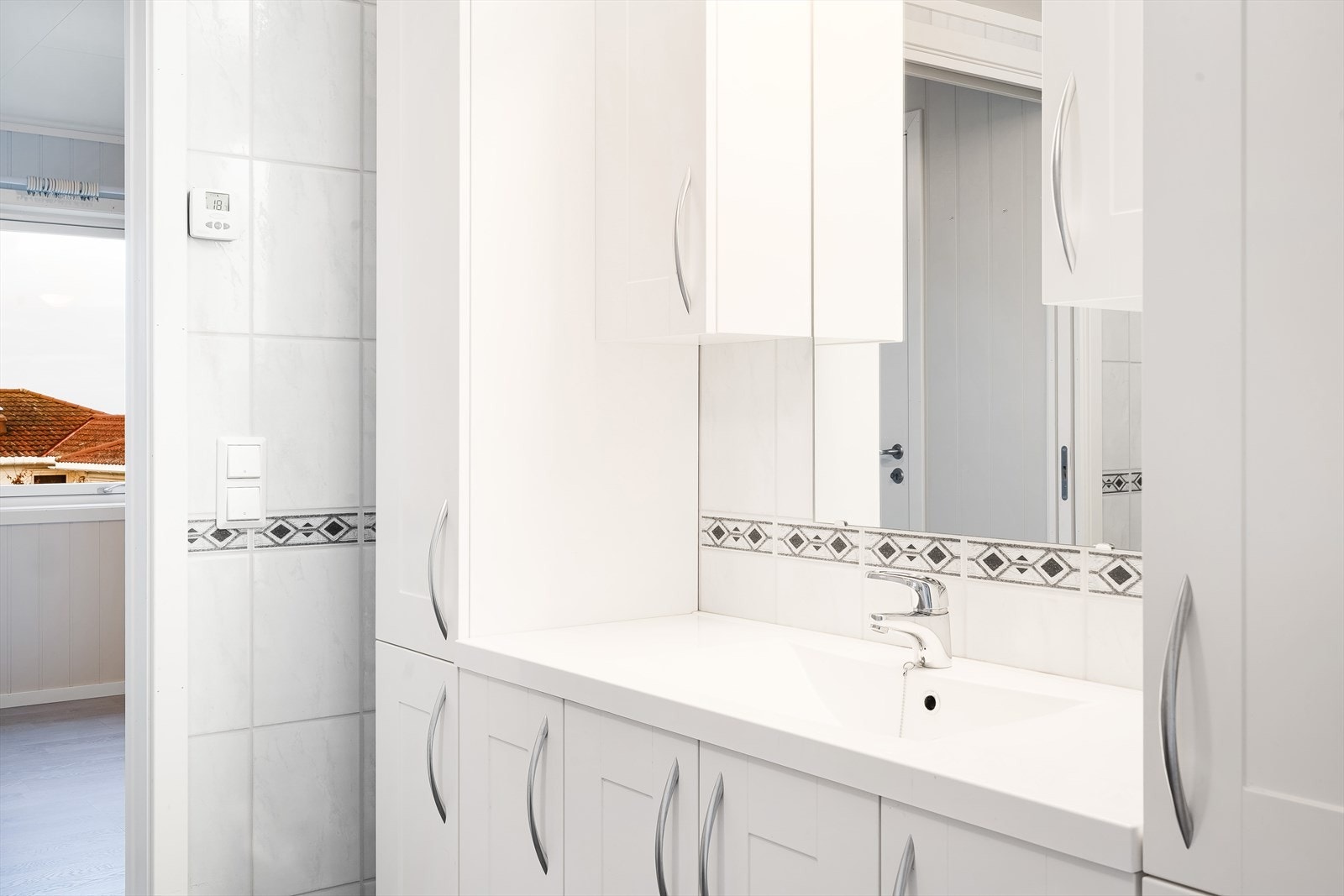 Badet har innredning med underskap, en vask, høyskap, overskap, speil og belysning. Galleribilde