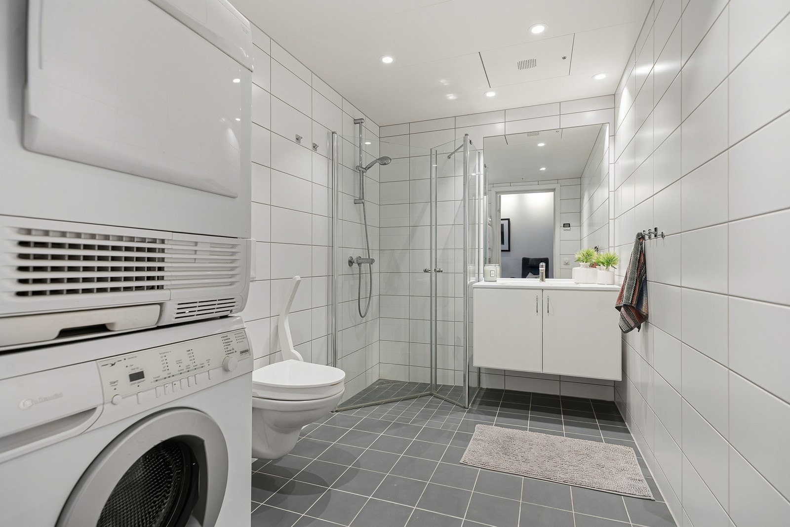 Flott baderom bestående av vegghengt toalett med støtte, baderomsinnredning og dusjhjørne med innfellbare dusjdører. Galleribilde