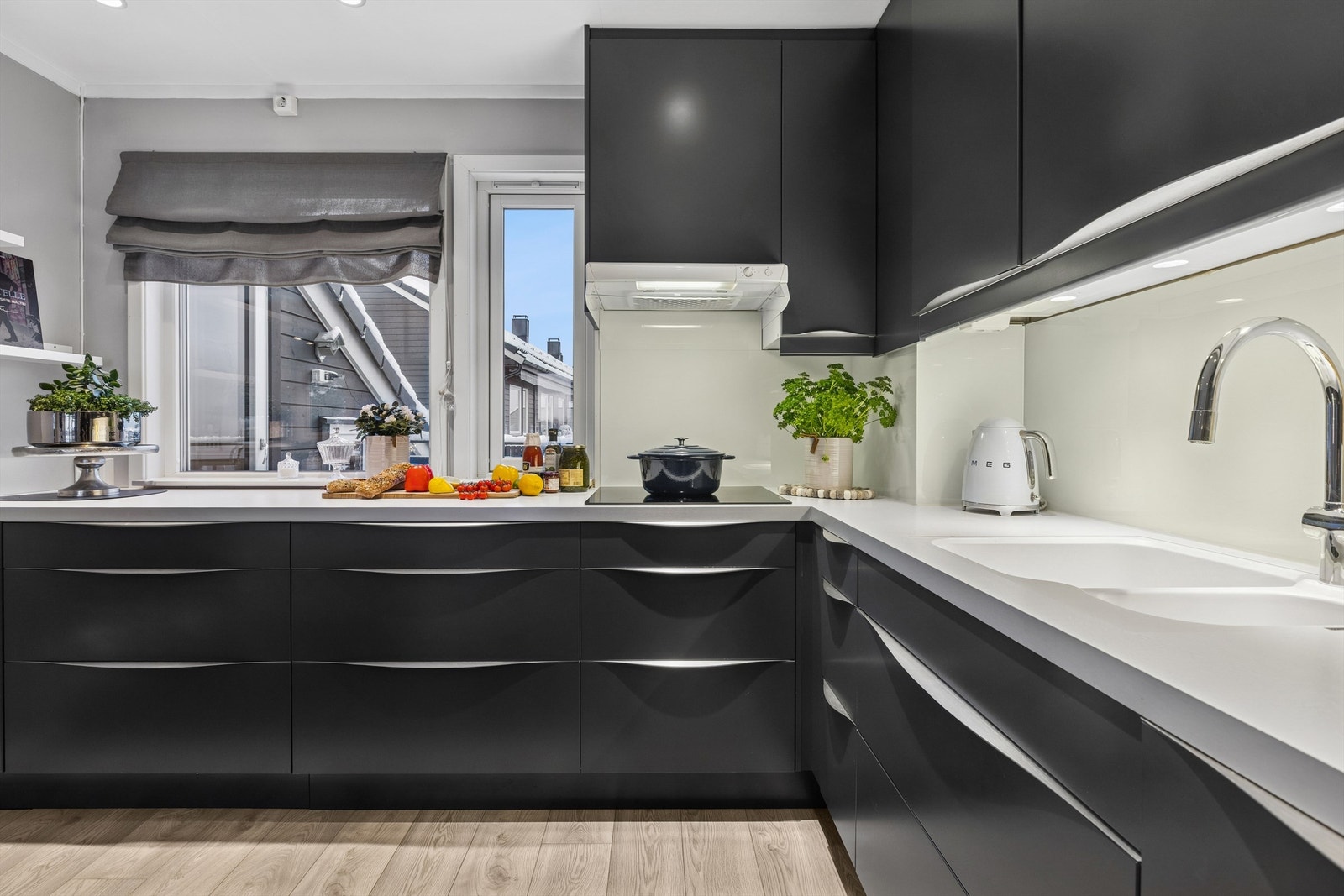 Epoq kjøkkeninnredning med glatte fronter og benkeplate av laminat med nedfelt oppvaskkum med ett-greps kjøkkenarmatur. Det er montert glassplate mellom kjøkkenbenk og overskap bak oppvaskkum, samt benkeskapsbelysning og stikkontakter over kjøkkenbenk. Galleribilde