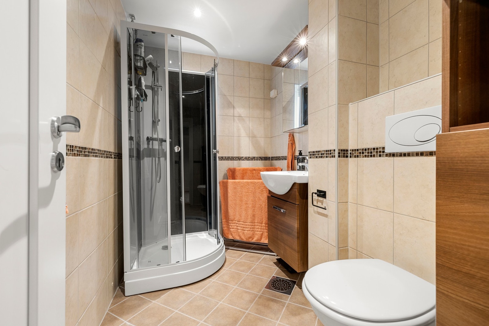 Baderommet er flislagt og utstyrt med vegghengt toalett, servant med skuffer, speil og dusjkabinett. Galleribilde