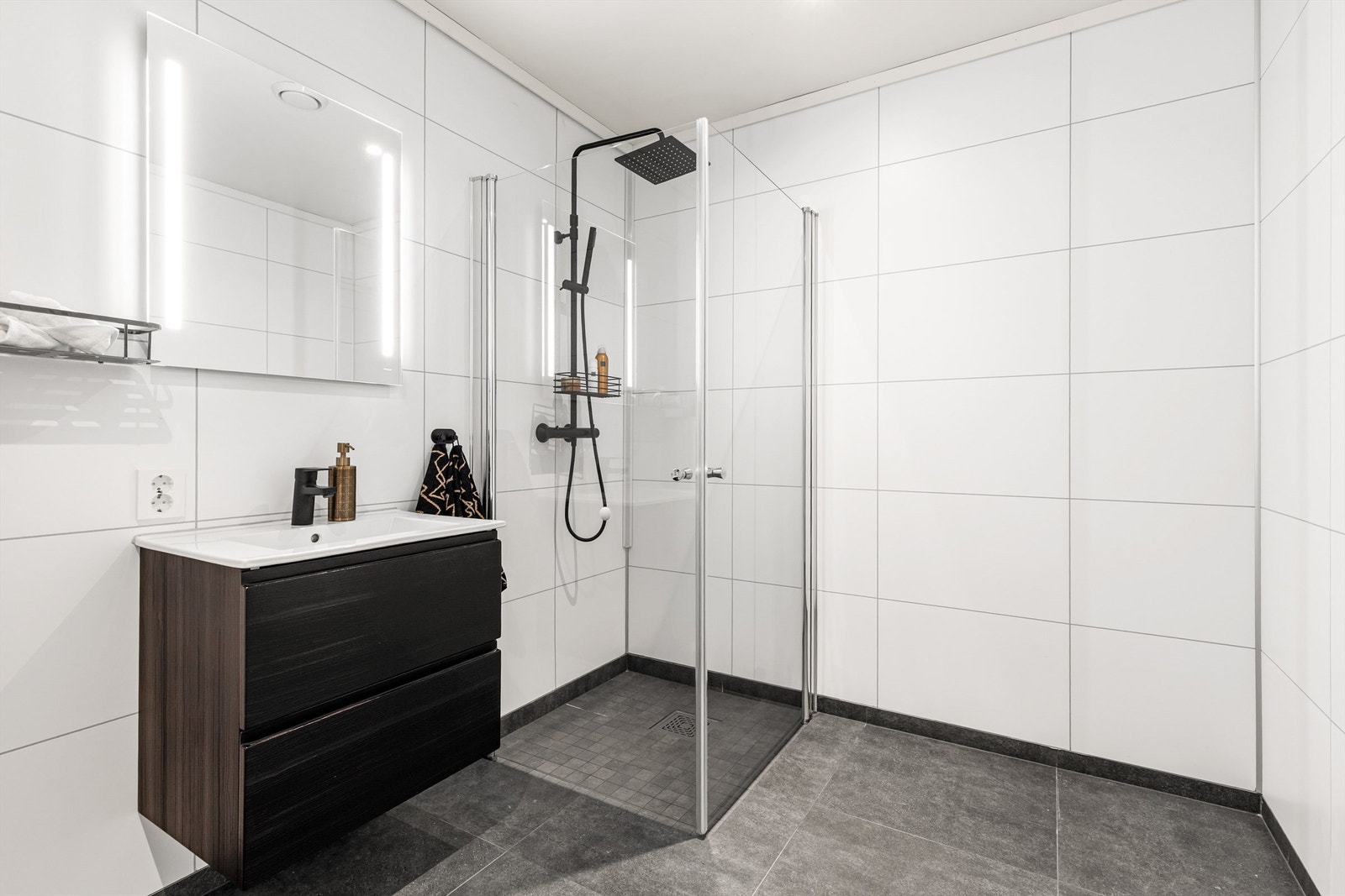 Vegghengt servantskap med ovenpåliggende servant og ett-greps armatur. Speil med integrert belysning over servant. Stikkontakt på vegg. Galleribilde