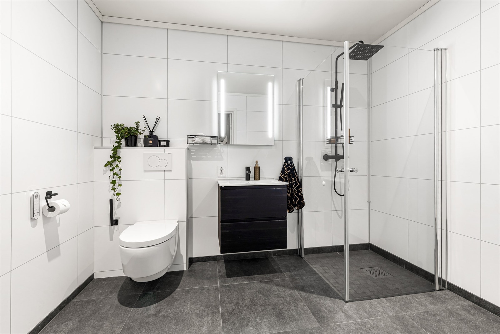 Bad fra byggeår. Flislagt gulv med varme. Baderomsplater på vegger. Himling av malt flate med downlights. Nedsenket dusjsone med innfellbare glassdører. Dusjarmatur tilkoblet hånddusj og regndusj. Galleribilde