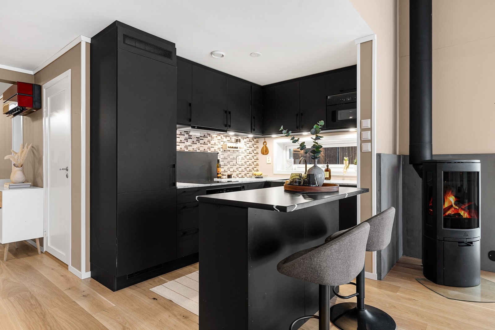 Laminerte benkeplater. Oppvaskkum med ett-greps armatur. Malt flate mellom benkeplate og overskap. Overbelysning og stikkontakter over benk. Integrerte hvitevarer. Galleribilde