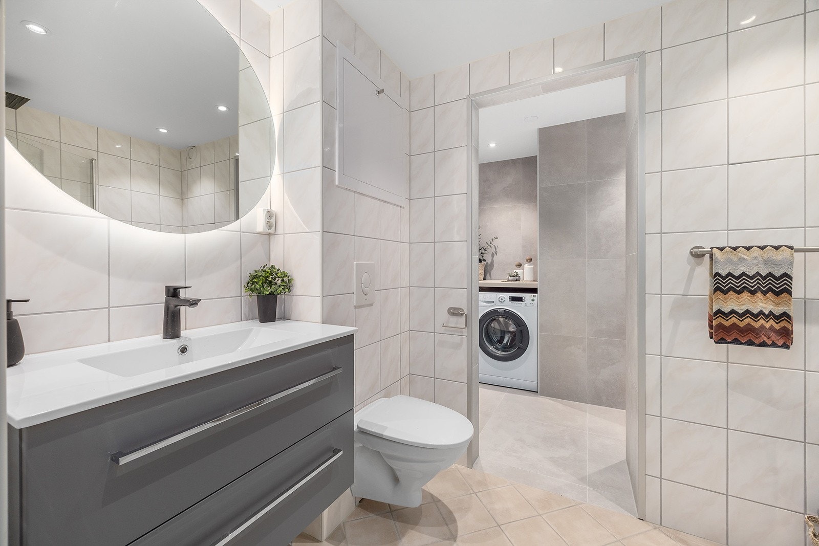 Moderne bad som består av servantinnredning med skuffer, speil m/belysning, dusjhjørne med hengslede glassvegger og veggmontert WC. Galleribilde