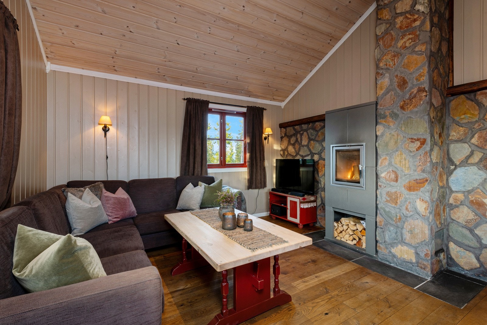 Parkettgulv kombineres med panelvegger malt i en dus jordtone, og etter en lang dag ute kan man komme inn for å varme seg foran en peisovn. Galleribilde