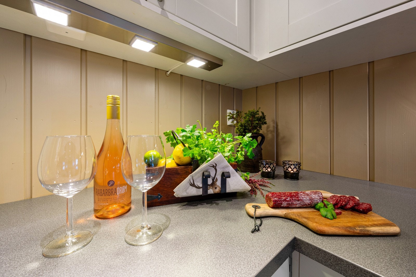 Her er det hvite, profilerte fronter og laminert benkeplate med nedfelt oppvaskkum. Over benken er det belysning, og over kokesonen er ventilator installert. Galleribilde