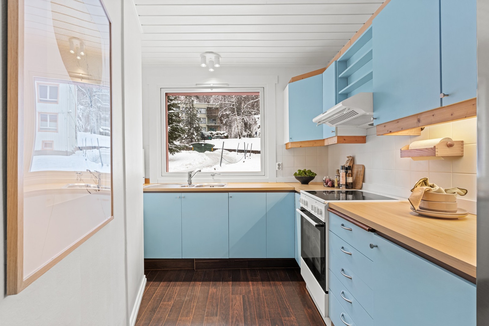 Kjøkkenet har en praktisk innredning med glatte, malte fronter og laminat benkeplate med nedfelt kum i rustfritt stål. Galleribilde