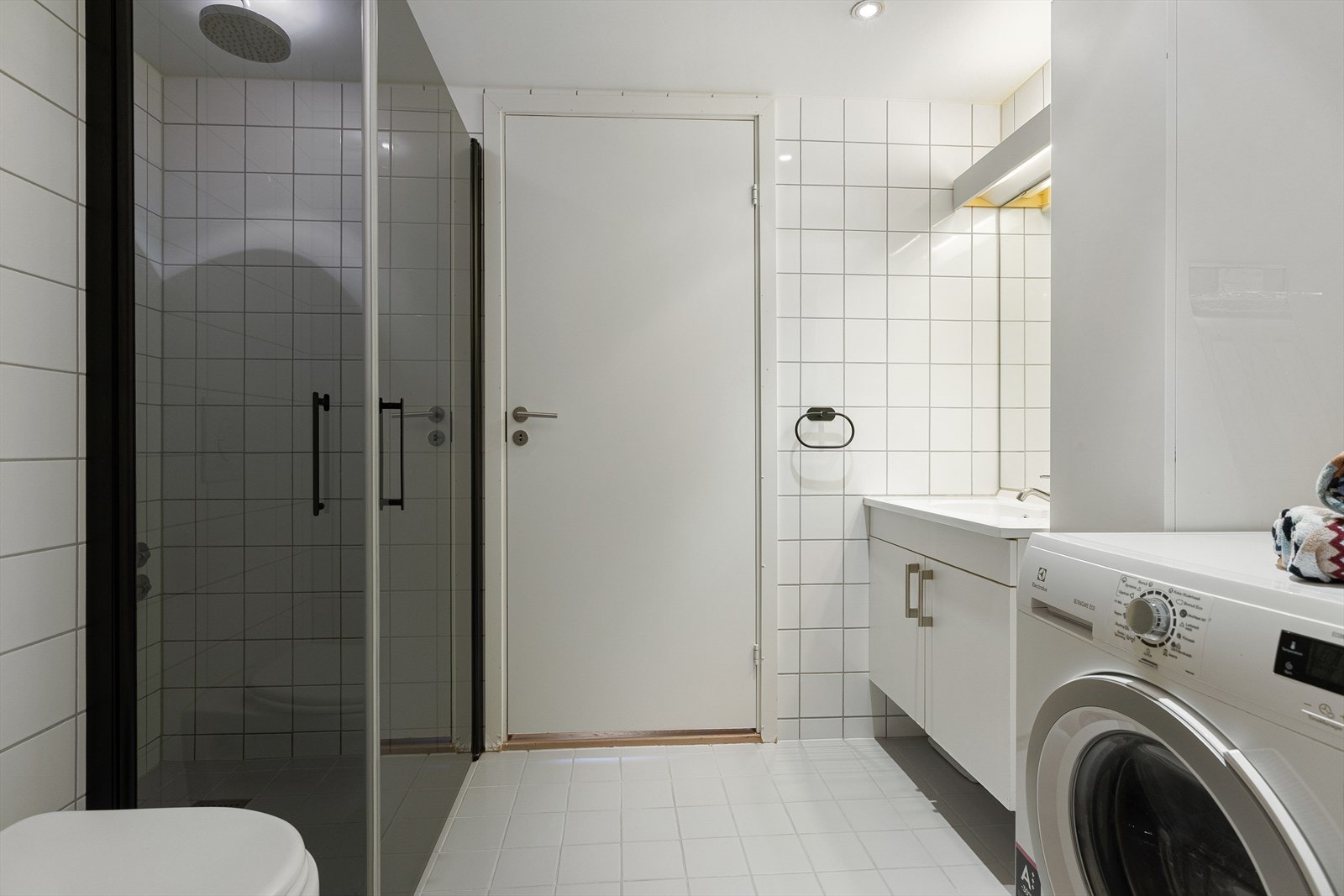 Flislagt baderom med elektriske varmekabler i gulv. Det er servant med underskap og opplegg for vaskemaskin Galleribilde