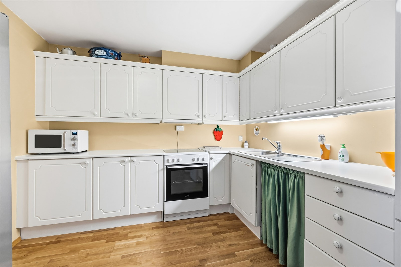 Kjøkkeninnredning med hvite, profilerte fronter og laminat benkeplate. Galleribilde