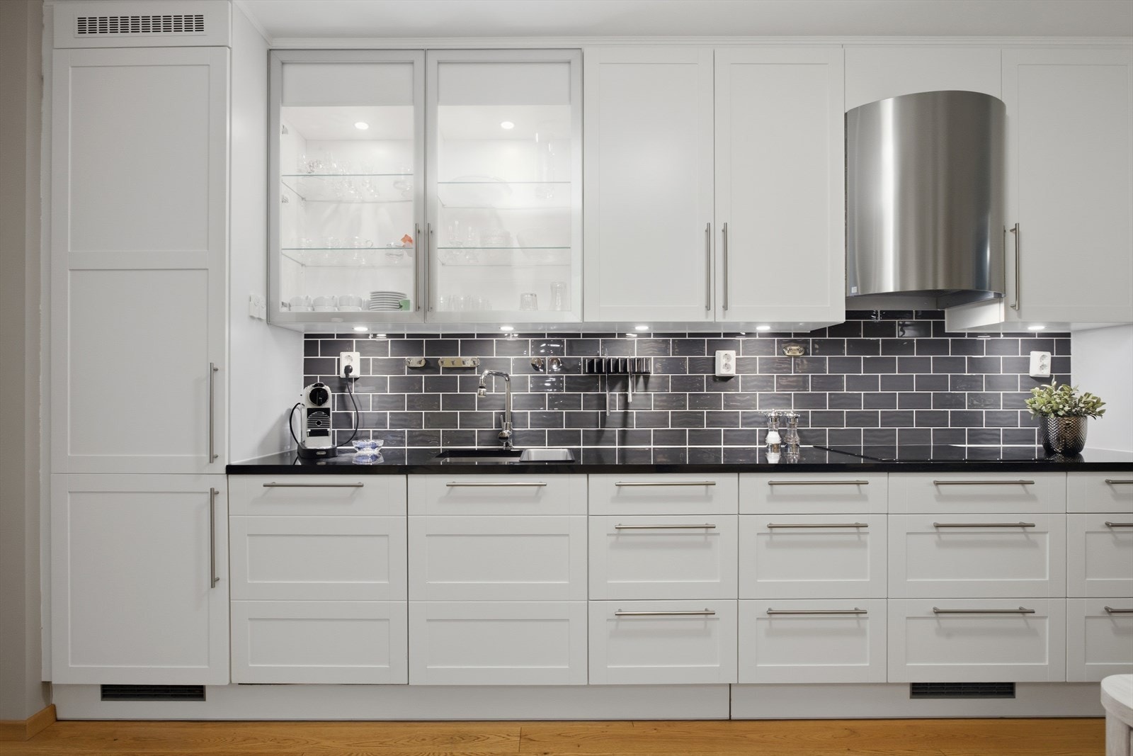 Underlimt oppvaskkum gir et moderne uttrykk og gjør renholdet enklere og mer praktisk. Mellom over-/underskap er det fliser som gir god beskyttelse. Flere underskap med kolonialskuffer og innfelte LED-lys i overskap med glass-/vitrineskapsdører. Galleribilde