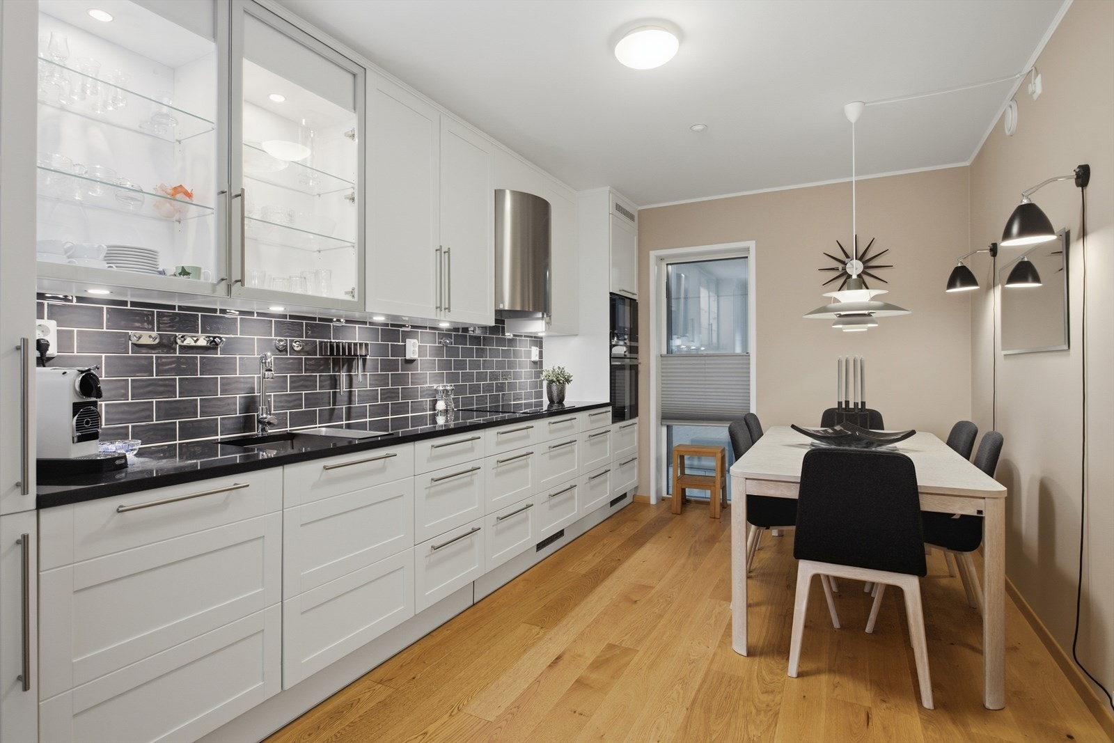 Innholdsrikt rom med innredning i hvit utførelse med dører fra produsenten Arens. Her er det lagt vekt på detaljer som gir et eksklusivt preg, som blant annet takhøye overskap og benkeplater av naturstein. Galleribilde