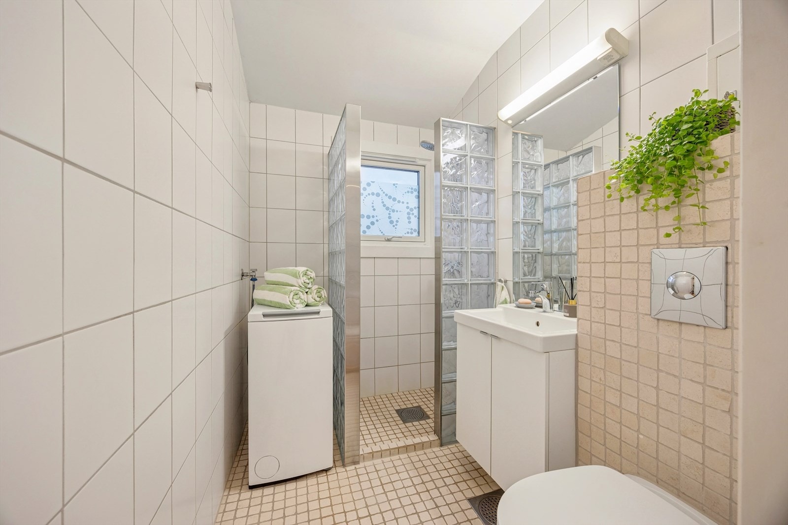 Badet er flislagt og innredet med dusjnisje av glassbyggestein, veggmontert toalett og servant med skap. Det er også opplegg for vaskemaskin. Galleribilde