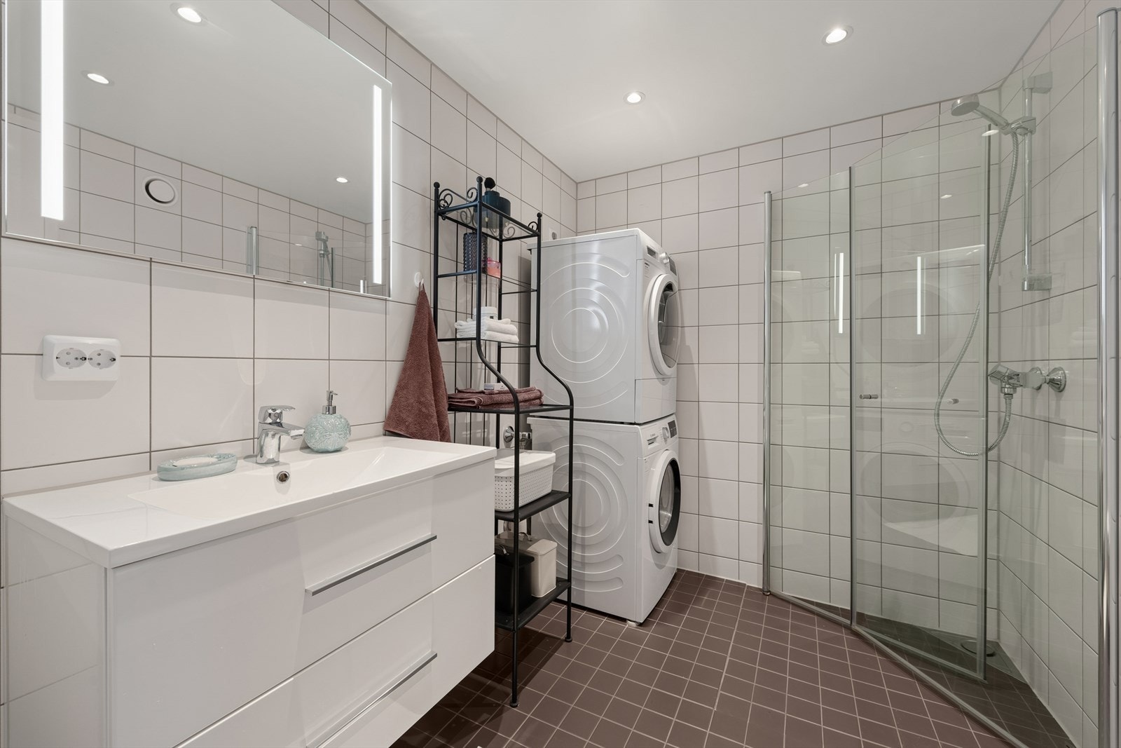 Baderommet har flislagt gulv med varmekabler. Dusjhjørne med innfellbare dører og opplegg til vaskemaskin gir et moderne bad med høy funksjonalitet. Galleribilde