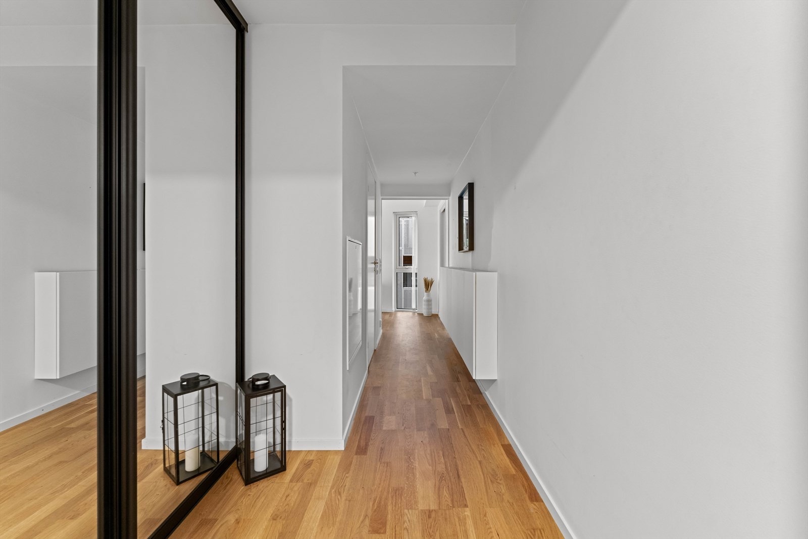 Entreen har plassbygget skyvedørsgarderobe med speilfronter og sort omramming, samt et hvitt, vegghengt oppbevaringsmøblement. Galleribilde