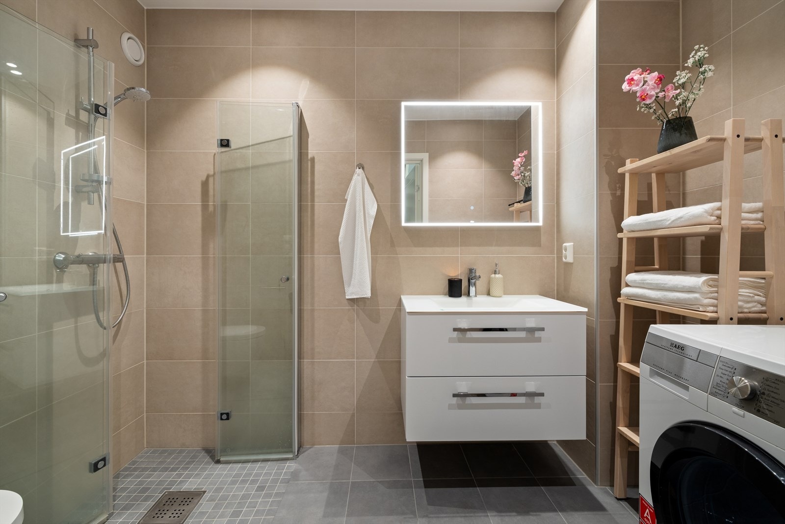 Badet i 2. etasje holder moderne standard med flislagte vegger og gulv for et stilrent uttrykk. Innredningen består av servant med oppbevaring, veggmontert toalett og dusjhjørne samt opplegg for vaskemaskin. Galleribilde