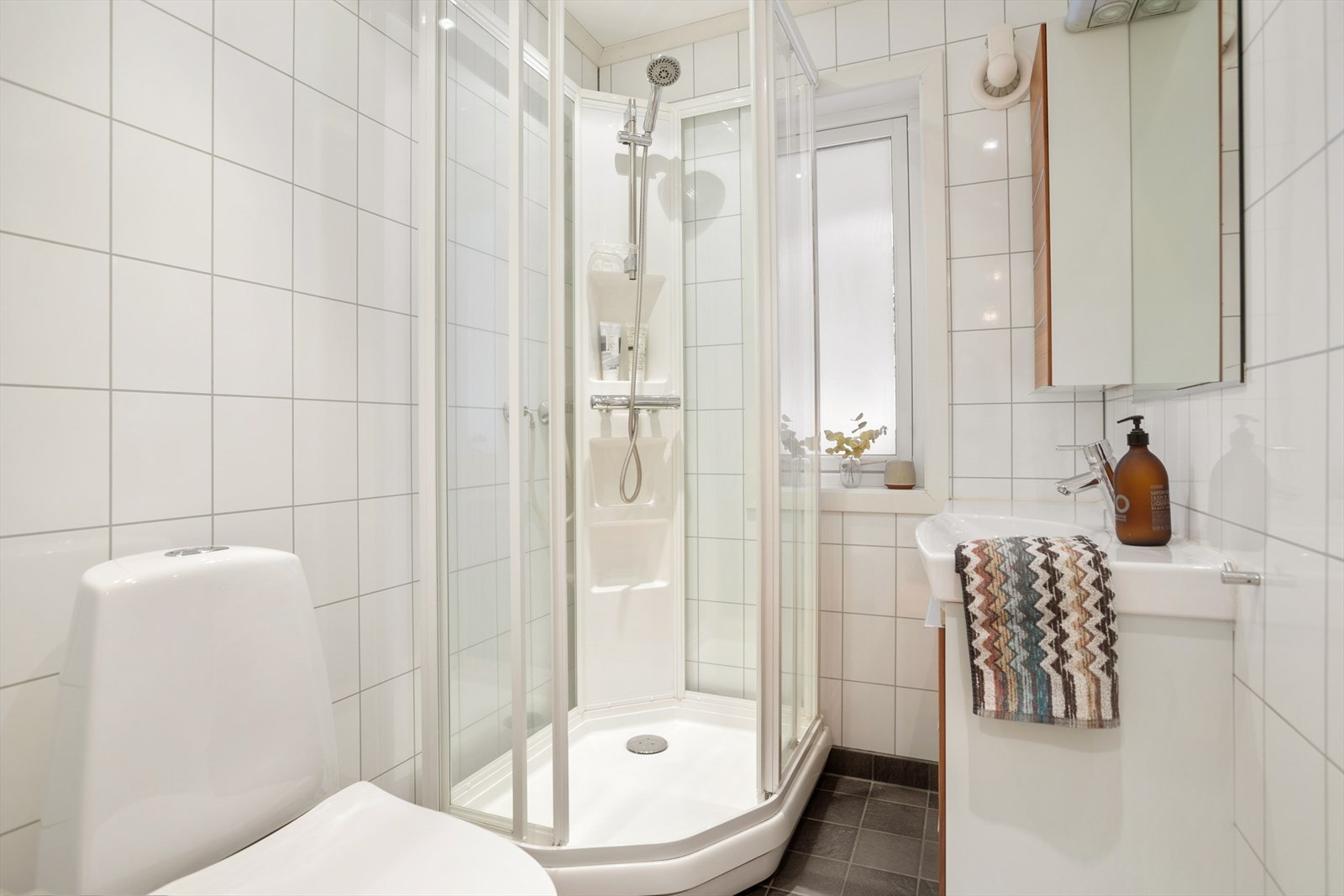 Baderommet i 1. etasje er innredet med servantskap med nedfelt servant, veggskap med speil og belysning, gulvmontert toalett og dusjkabinett. Galleribilde