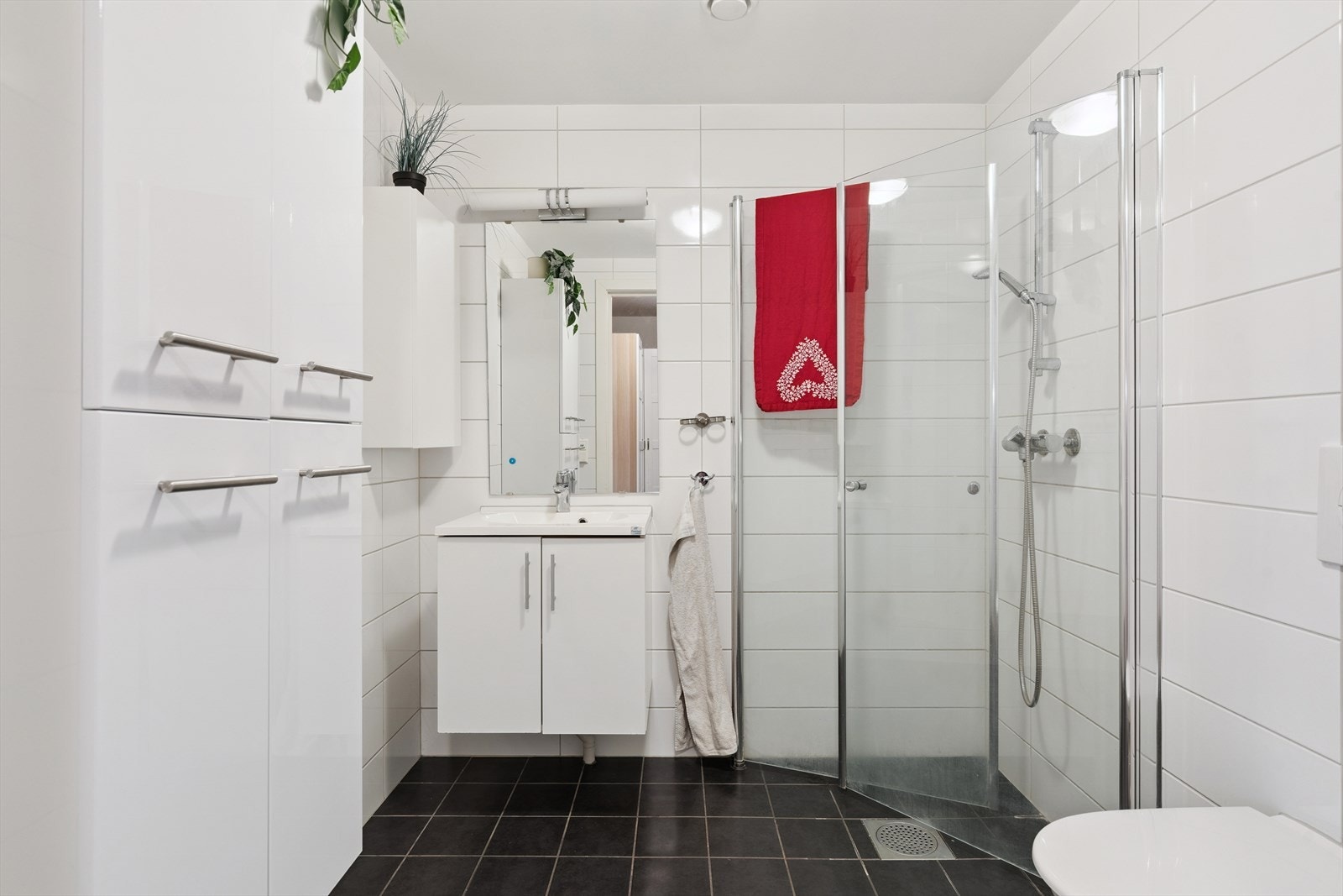 Badet er innredet med servantmøbel, vegghengt toalett og et dusjhjørne med innfellbare glassdører. Galleribilde