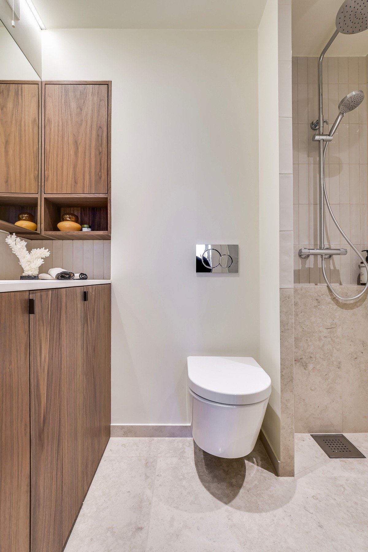 Et delikat uttrykk preger rommet, med lyse fliser i harmoniske toner på både gulv og vegger, som gir en rolig og tidløs atmosfære. Den mørke, snekkerbygde baderomsinnredningen står i stilfull kontrast og består av skapmodul med ovenpåliggende servant. Galleribilde