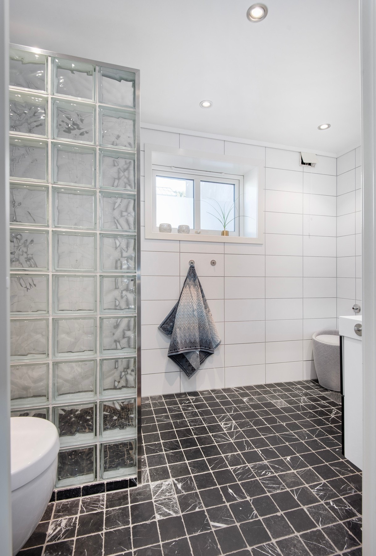 Helfliset bad fra 2009 med elektriske varmekabler. Innredet med vegghengt toalett, dusjhjørne med vegg i glassbyggerstein og glassdører. Galleribilde