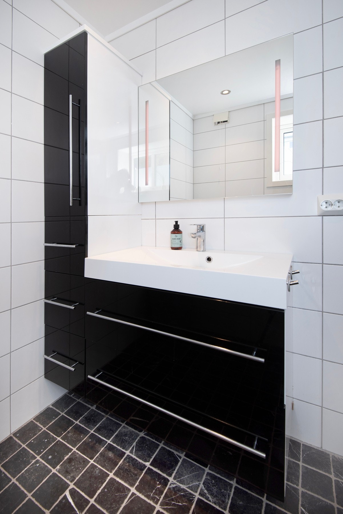 Servantinnredning med to mørke skuffer, helstøpt kompositt servantplate, speil med integrert belysning og et høyskap. Galleribilde