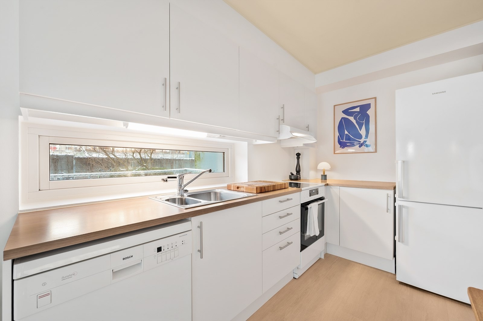 Kjøkkeninnredningen har hvite glatte fronter og laminat benkeplate. Galleribilde