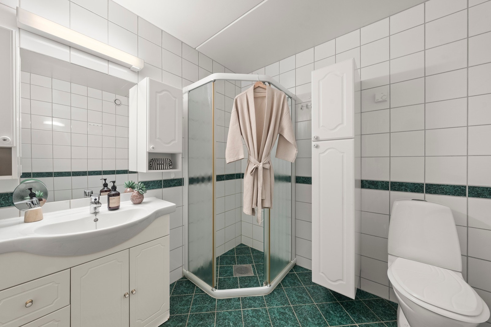 Rommet har flislagte vegger og gulv, servant med innredning, gulvstående toalett og dusjhjørne med dusjvegger. Det er også opplegg for vaskemaskin, noe som gir god praktisk funksjon. Galleribilde