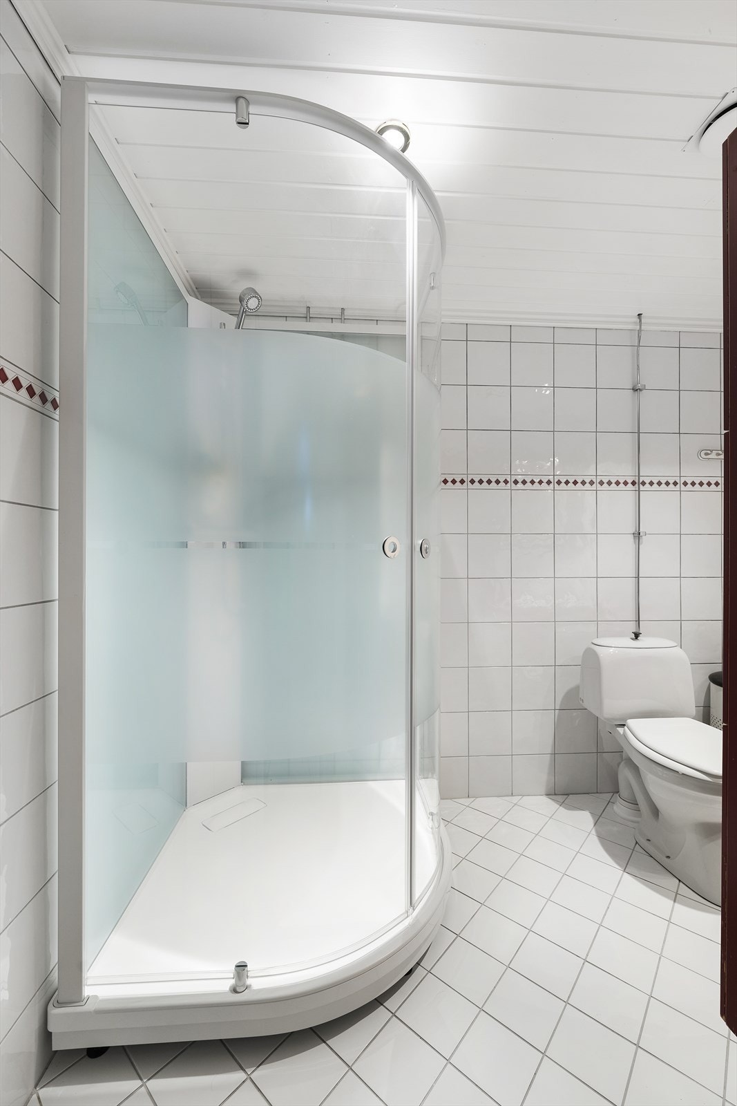 Badet er flislagt og innredet med dusjkabinett, sokkeltoalett og servantinnredning med praktisk oppbevaring. Galleribilde
