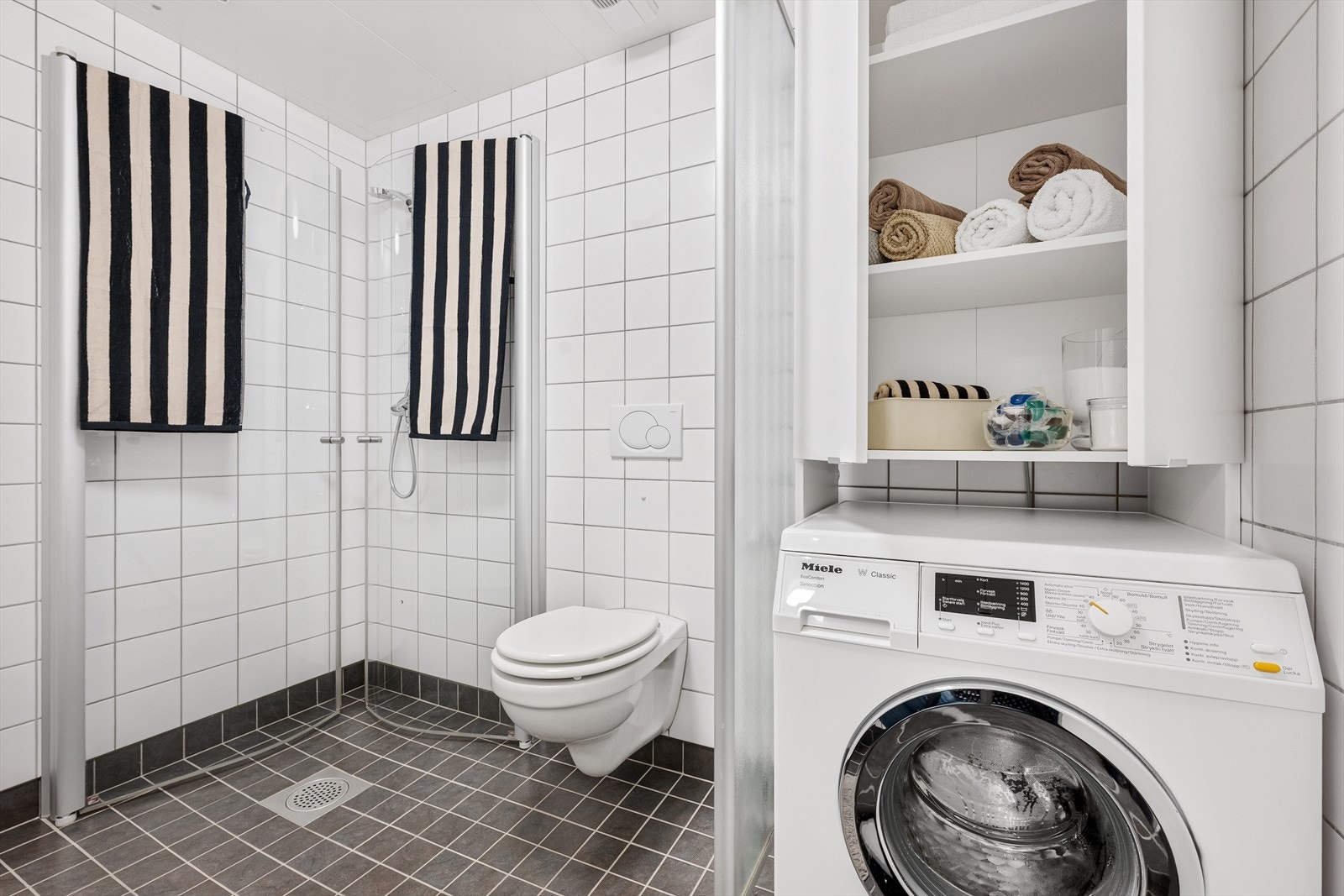 Badet er innredet med servant med underskap, speil på veggen og praktisk skapinnredning over vaskemaskinen. Galleribilde