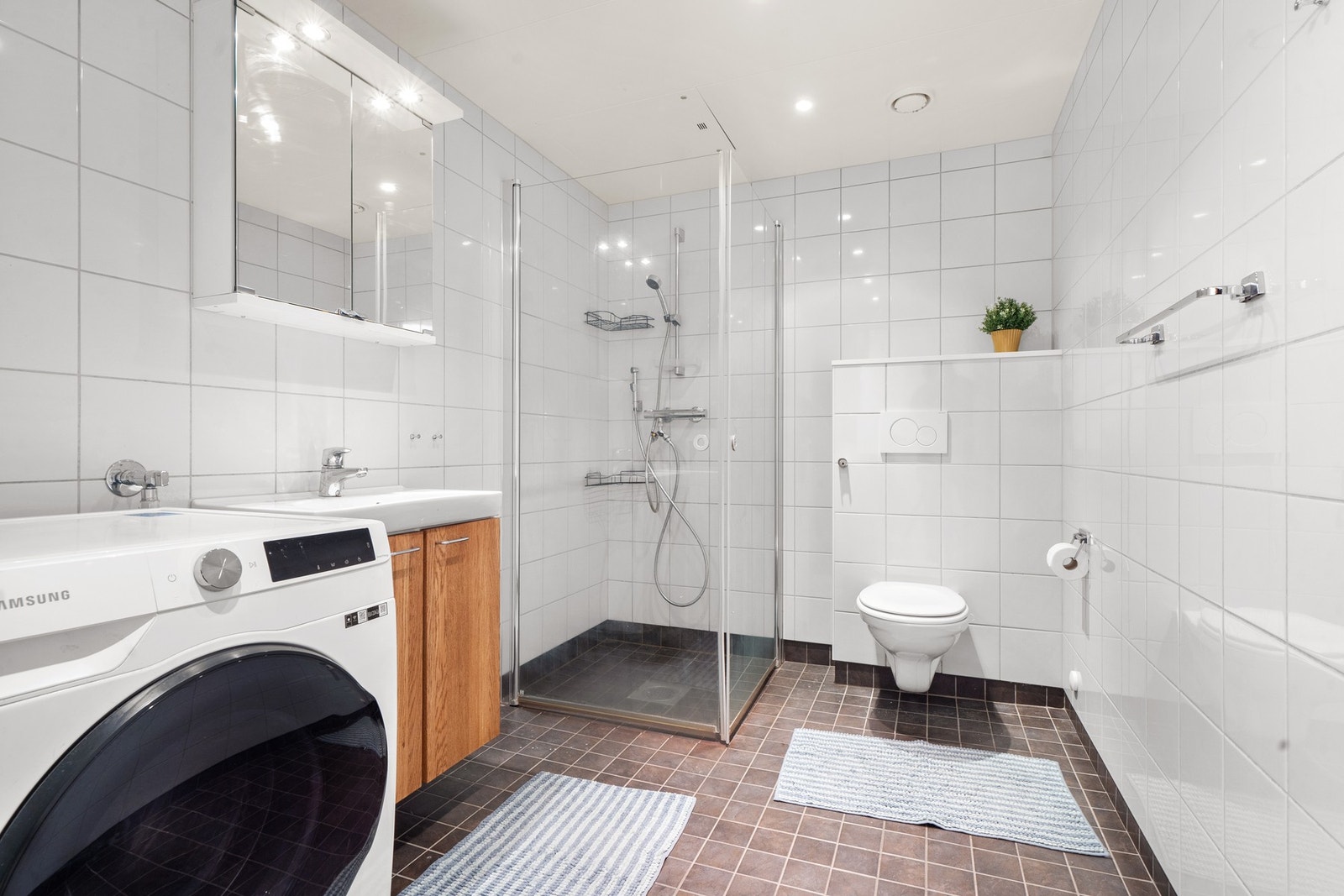 Romslig, flislagt bad med varme i gulv, dusjhjørne med inn-/utadslående glassdører, vegghengt toalett og servantseksjon med skuffer. Praktisk opplegg for vaskemaskin og avtrekk tilkoblet ventilasjonsanlegget. Galleribilde