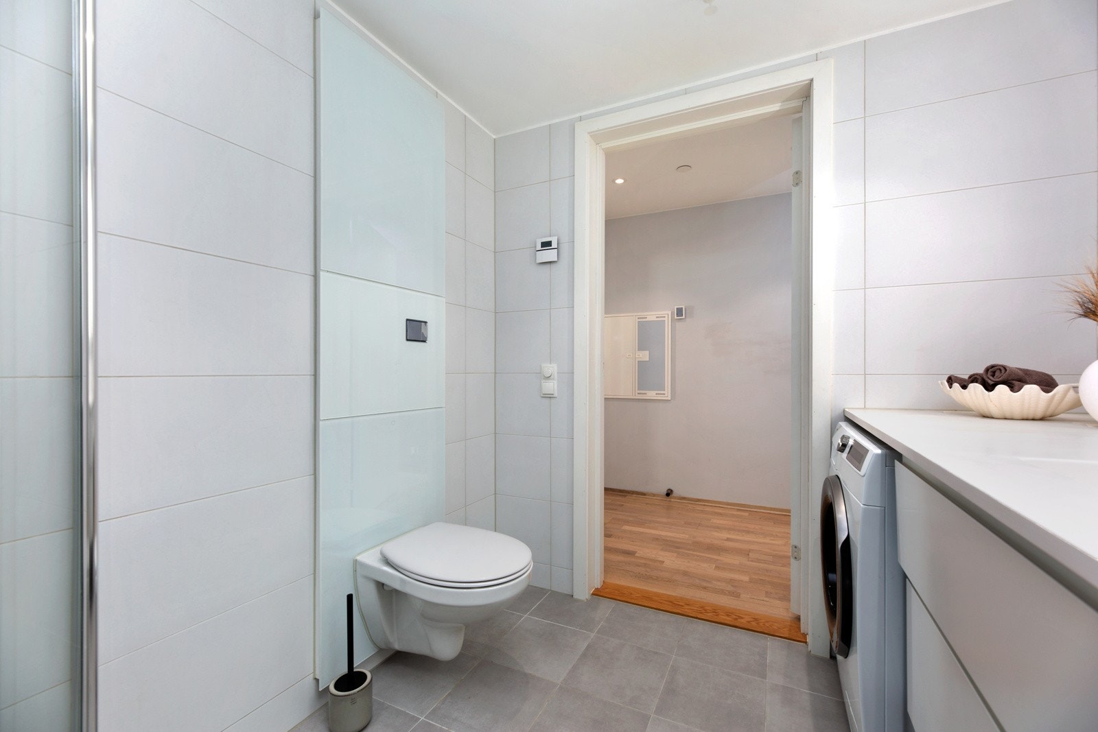 Rommet er innredet med servantskap med ovenpåliggende servant, speil med lys på vegg, dusjhjørne og vegghengt toalett, samt flislagte vegger og gulv. Galleribilde