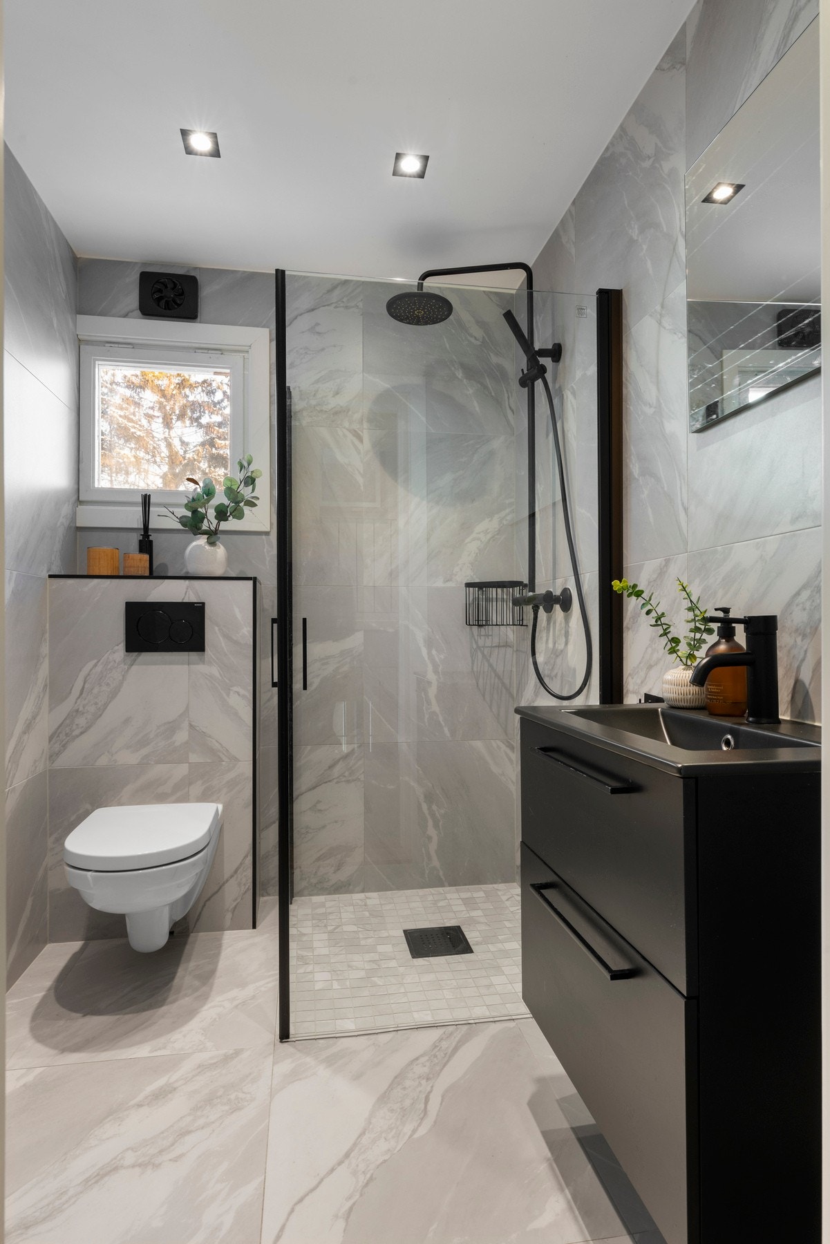 Begge har flislagte overflater og er utstyrt med vegghengt toalett, dusjhjørne med glassdører samt servant med tilhørende oppbevaring. Galleribilde