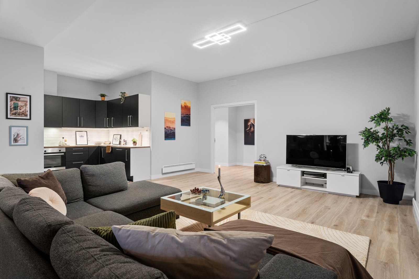 Stilren stue i åpen løsning mot kjøkkenet, med moderne uttrykk og god plass til både avslapning og sosiale sammenkomster. Galleribilde